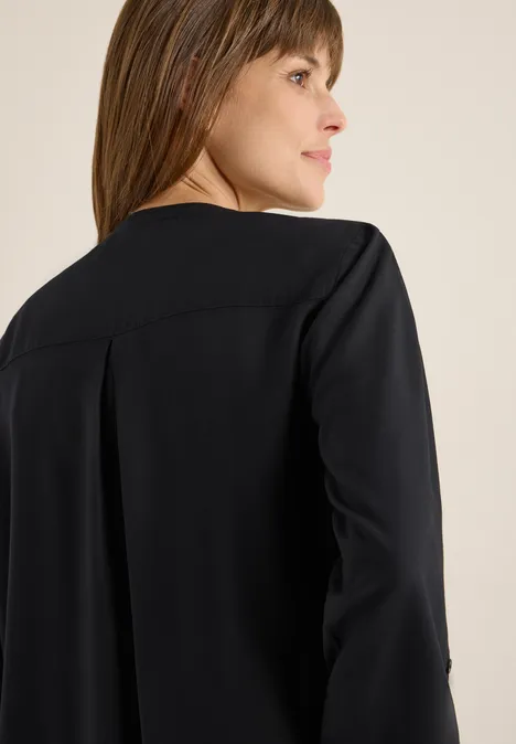 Frau mit braunen Haaren trägt eine schwarze Jacke und schaut zur Seite.